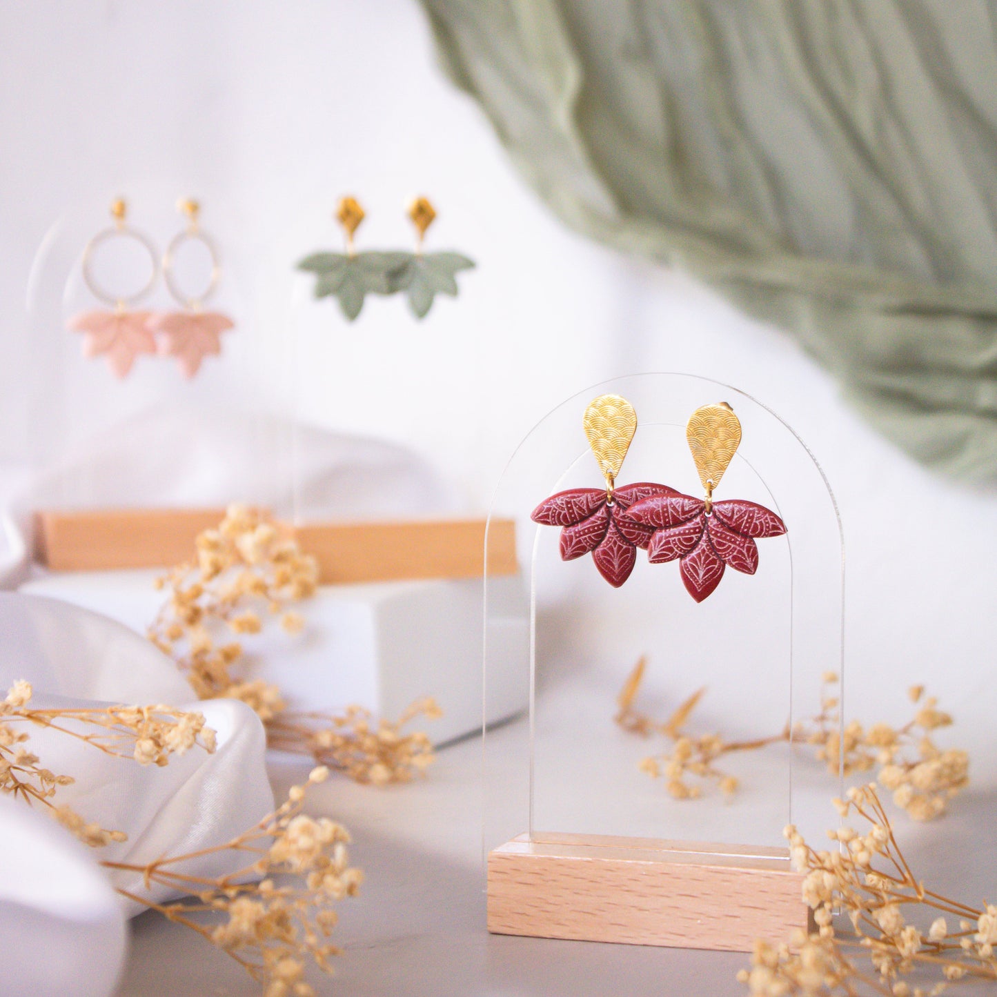 Earrings displayed on a stand with dried flowers and a blurred green curtain in the background