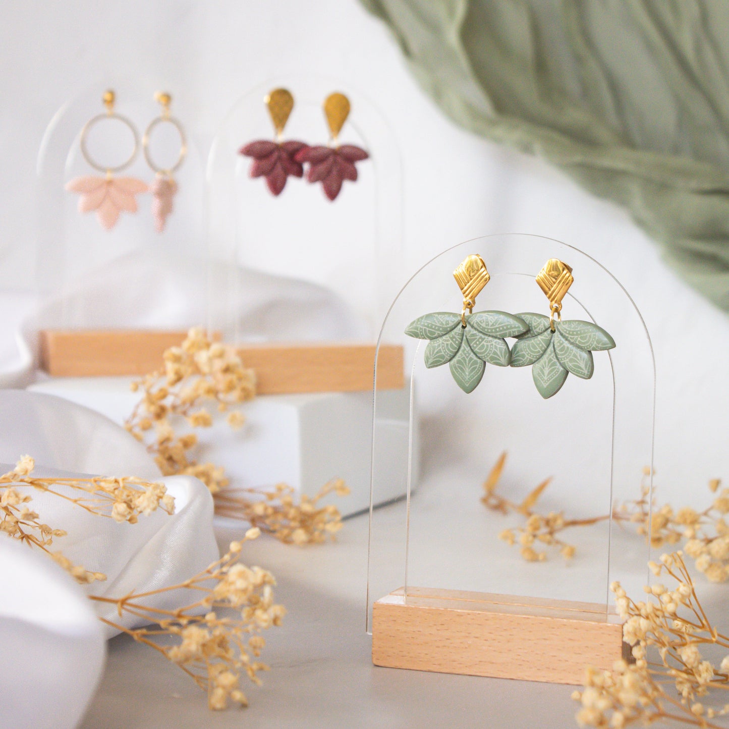 Earrings displayed on a stand with a white background and greenery.
