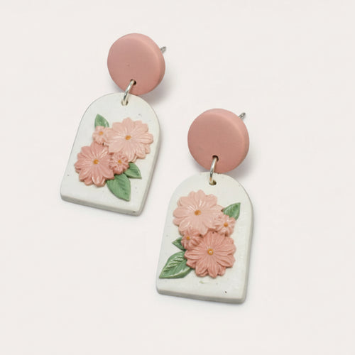 A pair of earrings featuring a speckled white and pink polymer clay base with handpainted floral details, arranged in an arch shape.