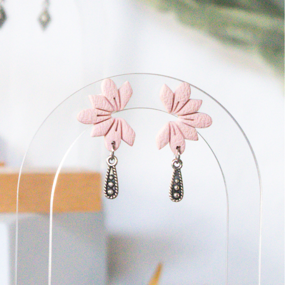 Pink floral earrings on a clear stand with a blurred background