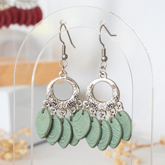 Silver earrings with green polymer clay charms on a clear stand.