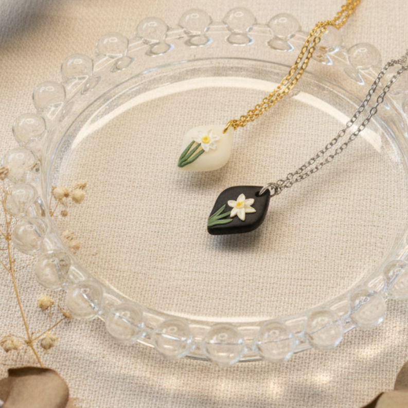 Two december birth flower necklaces on a clear glass plate with dried leaves and flowers around.