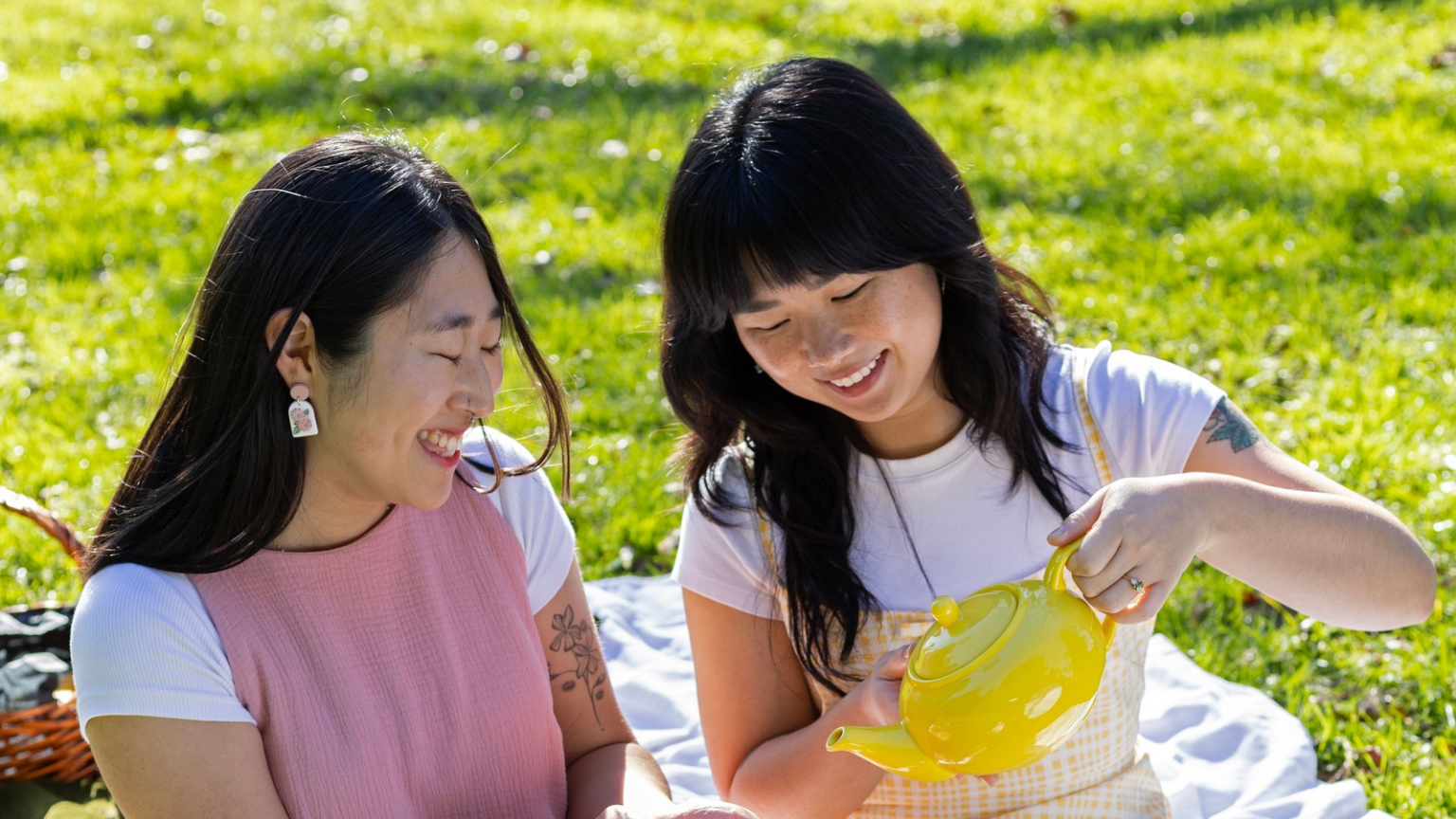 two women wearing handmade earrings by Arias Design Co sitting on a picnic blanket in New Zealand
